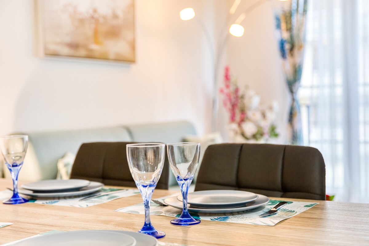 Et aussi — Table bois, verres bleus, vaisselle blanche, canapé gris, lumière douce