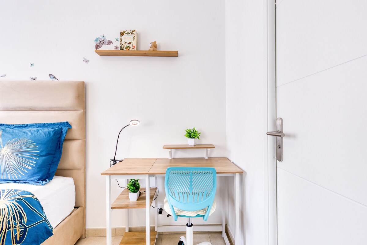 Chambres — Chambre moderne avec lit beige, bureau bleu, lumière naturelle