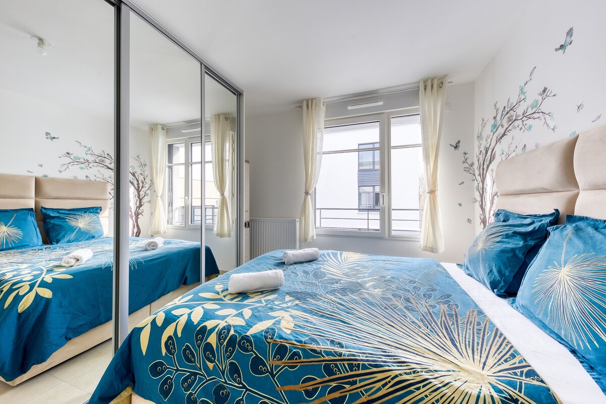 Chambres — Lit bleu motifs dorés, miroir mural, lumière naturelle abondante