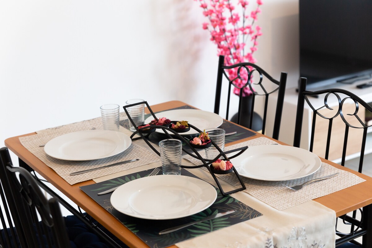 Cuisine — Table dressée, chaises noires, décoration florale rose