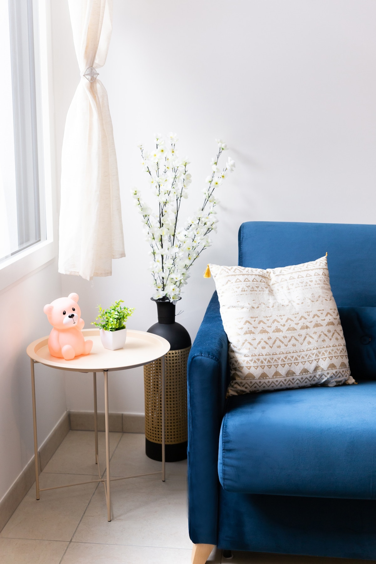 Chambres — Canapé bleu, coussins beiges, fleurs blanches, lumière naturelle douce