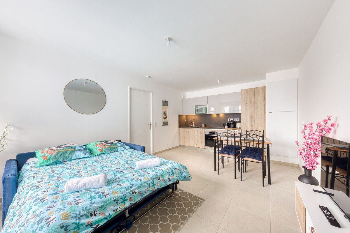 Chambres — Lit bleu avec draps colorés, cuisine ouverte visible, lumineux et spacieux